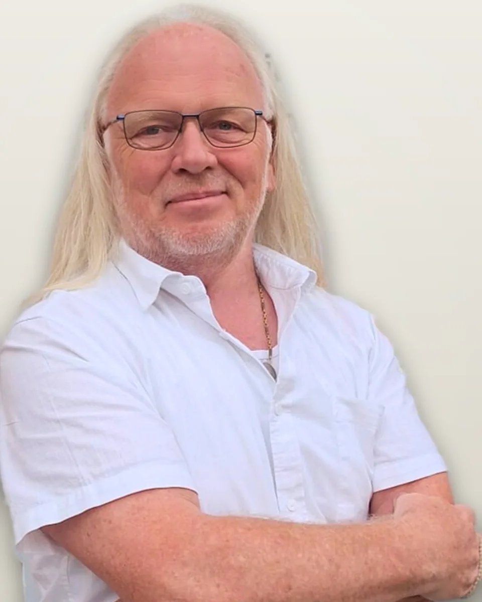 Ralf Schwarz, Portrait vor hellem Hintergrund, im hellen Kurzarmhemd mit verschränkten Armen.